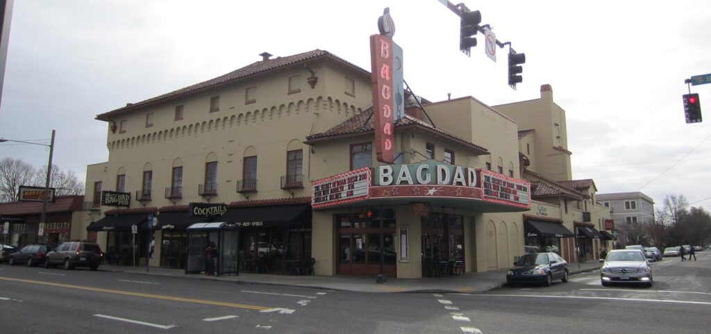 A historic Spanish-style theater with a tall vertical Bagdad sign and marquee on a street corner
