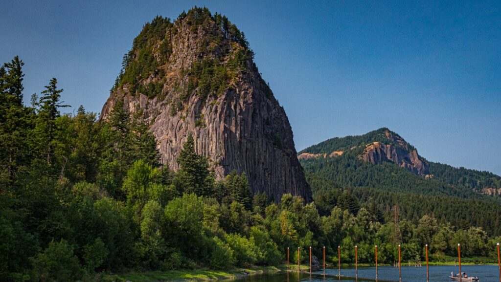 The dark volcanic monolith of Beacon Rock rising above forest on the Columbia River's Washington shore
