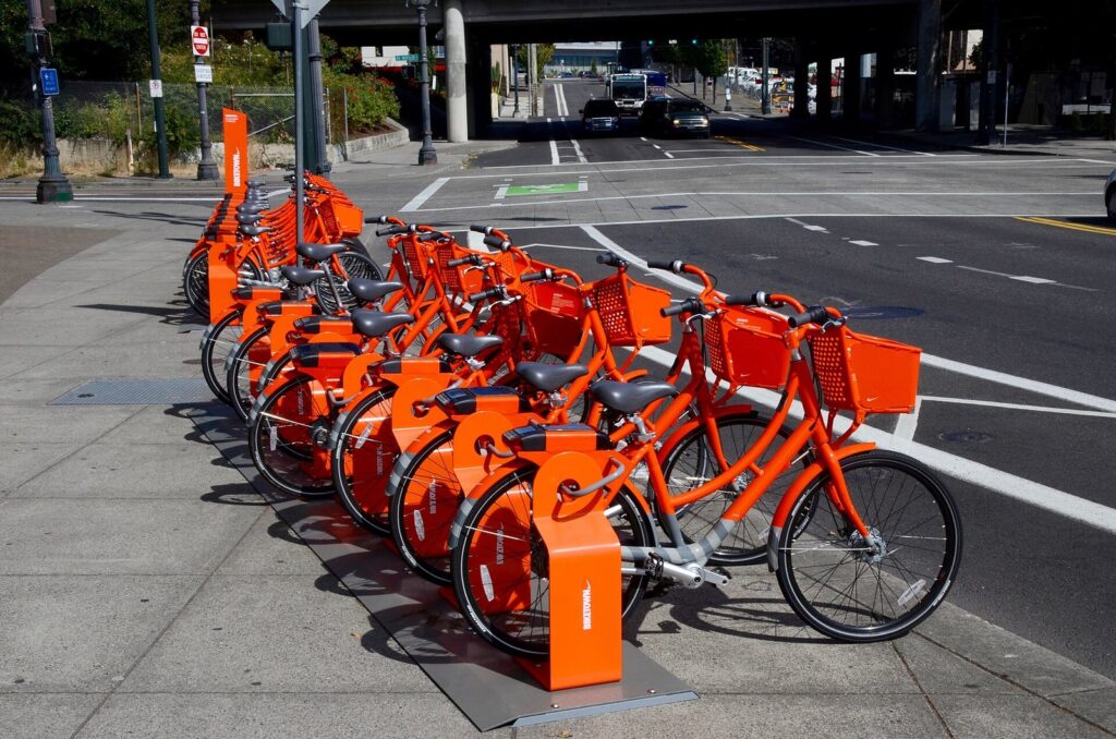 A row of orange BIKETOWN bikes docked at a station on a downtown Portland sidewalk