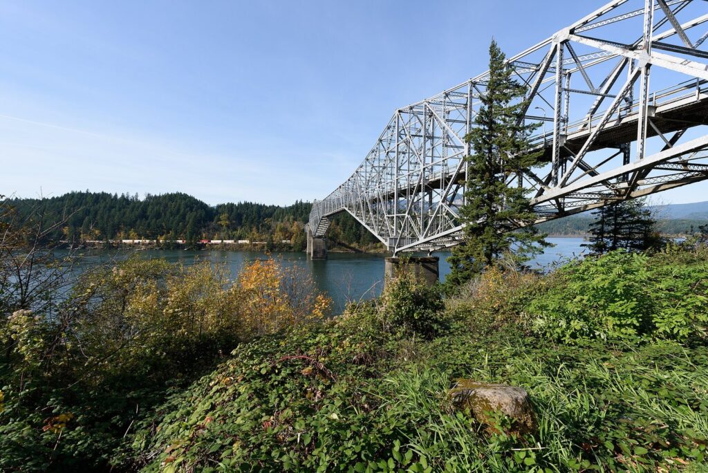 The steel truss Bridge of the Gods spanning the Columbia River beside tall firs and autumn brush