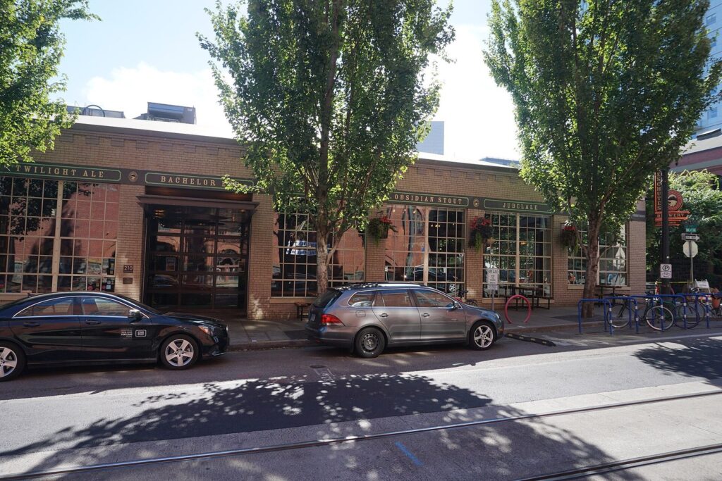 A brick brewpub with large arched windows, hanging flower baskets and street trees on a Pearl District corner