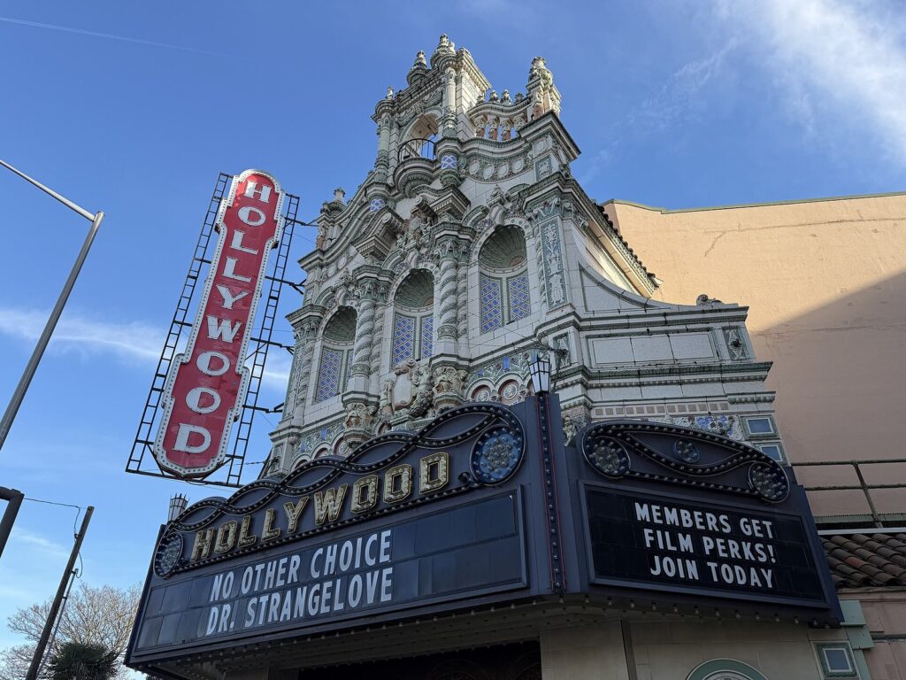 The ornate terra-cotta facade, vertical Hollywood sign and marquee of the Hollywood Theatre against a blue sky