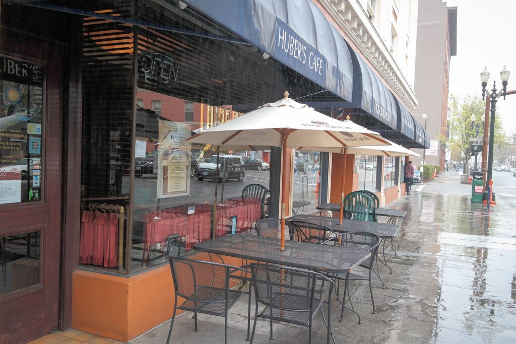The awning and sidewalk tables of Huber's Cafe on a rain-soaked downtown street