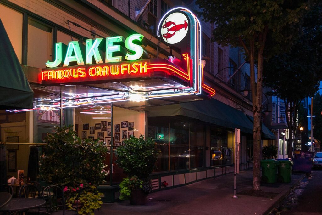 The green and red neon sign of Jake's Famous Crawfish glowing over its entrance at dusk