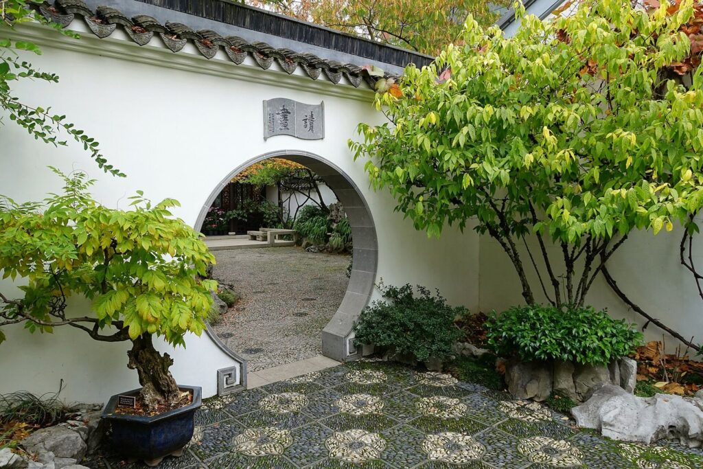 A round moon gate in a white wall at Lan Su Chinese Garden, framing a courtyard and a potted tree