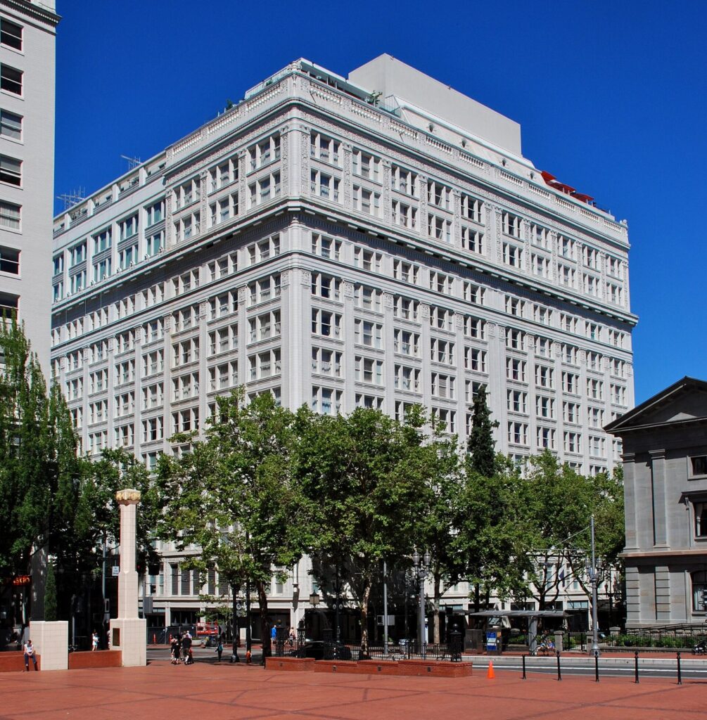 The white terra-cotta Meier and Frank Building rising above the brick plaza of Pioneer Courthouse Square on a sunny day