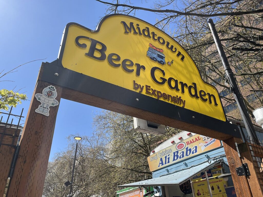 The yellow arched sign of Midtown Beer Garden over the pod entrance, with food carts behind it