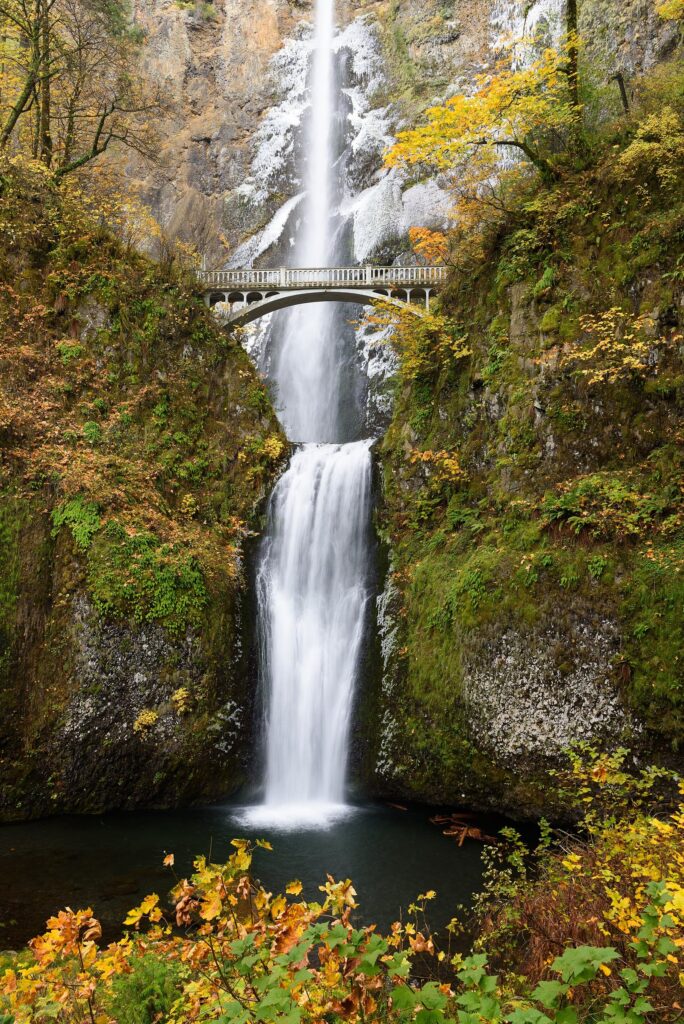 Multnomah Falls dropping in two tiers past the Benson Bridge, framed by autumn leaves