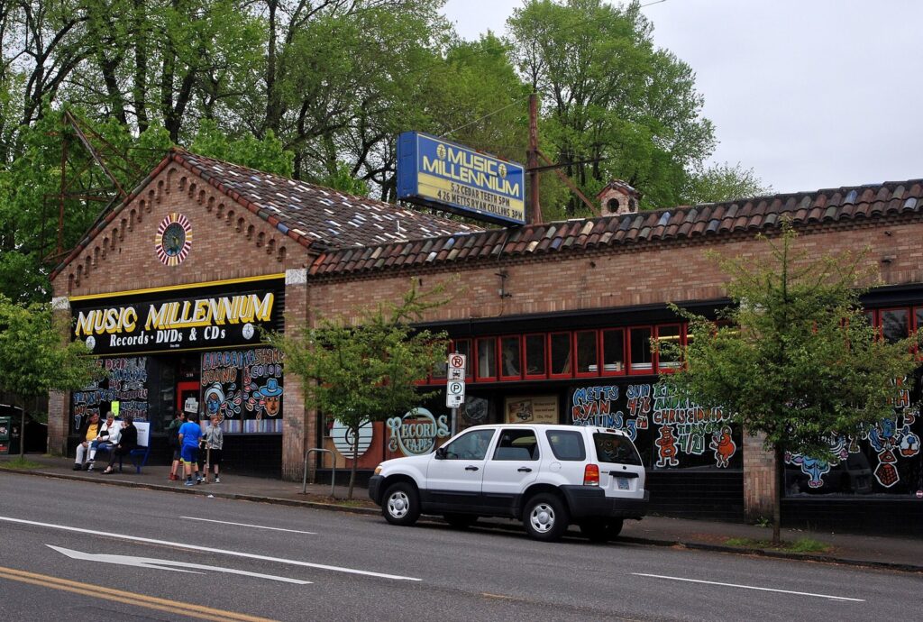 A long brick storefront with a Music Millennium sign and painted windows on a tree-lined street