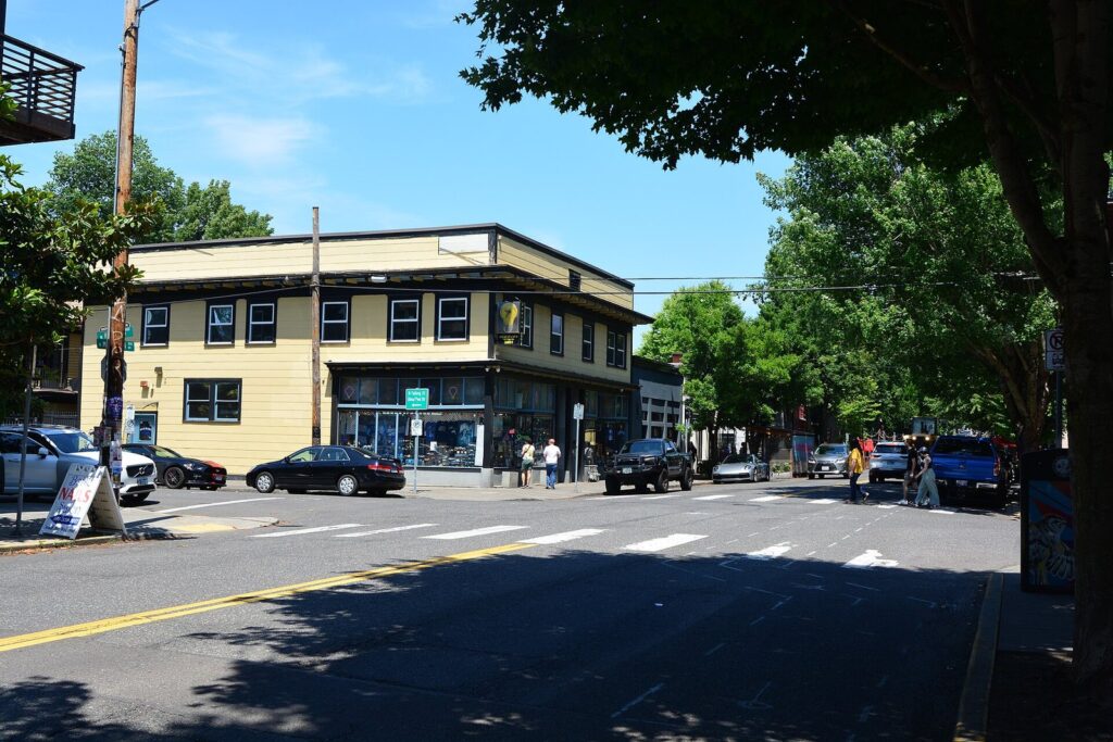 A two-story corner building with shopfronts at N Mississippi Avenue and Failing Street, shaded by street trees