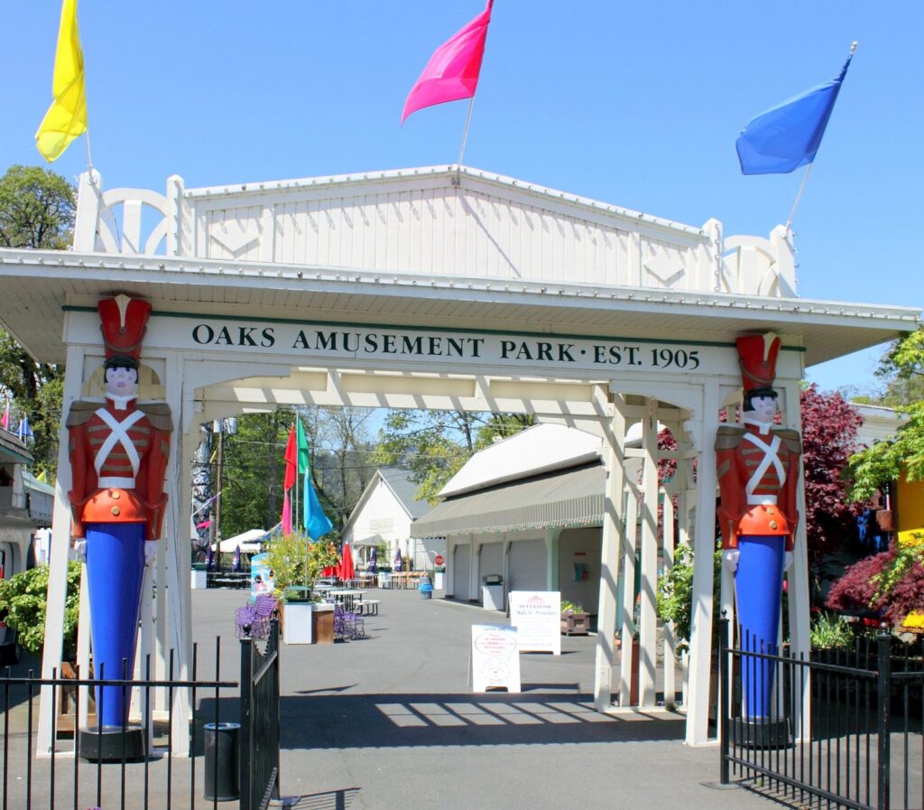 The white entrance arch of Oaks Amusement Park with its Est. 1905 sign and two toy soldier statues