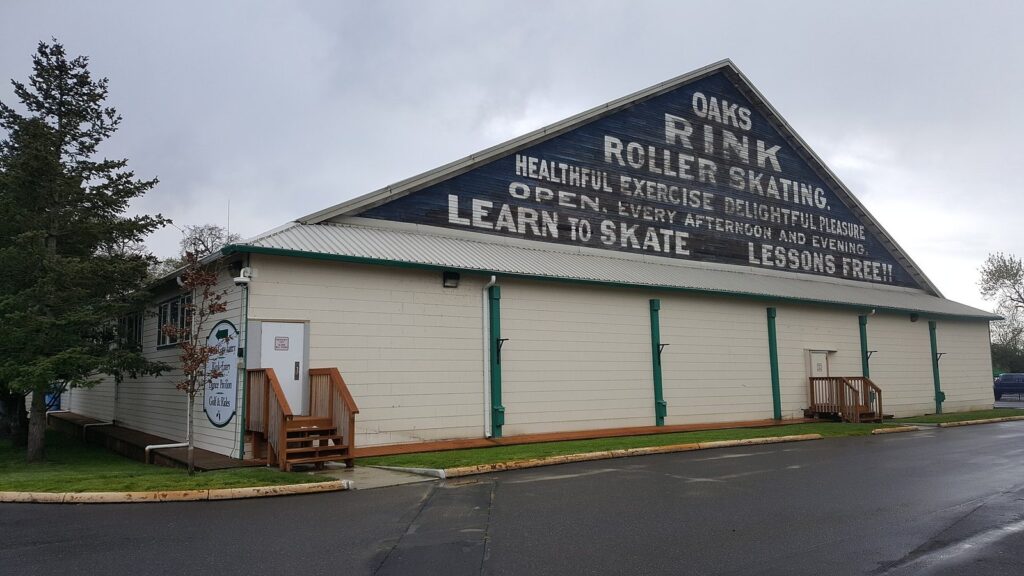 The white wooden hall of the Oaks Park roller rink with a painted gable sign advertising roller skating and free lessons