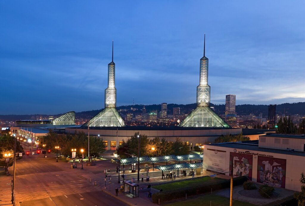 The twin glass spires of the Oregon Convention Center lit at dusk, with downtown's towers behind