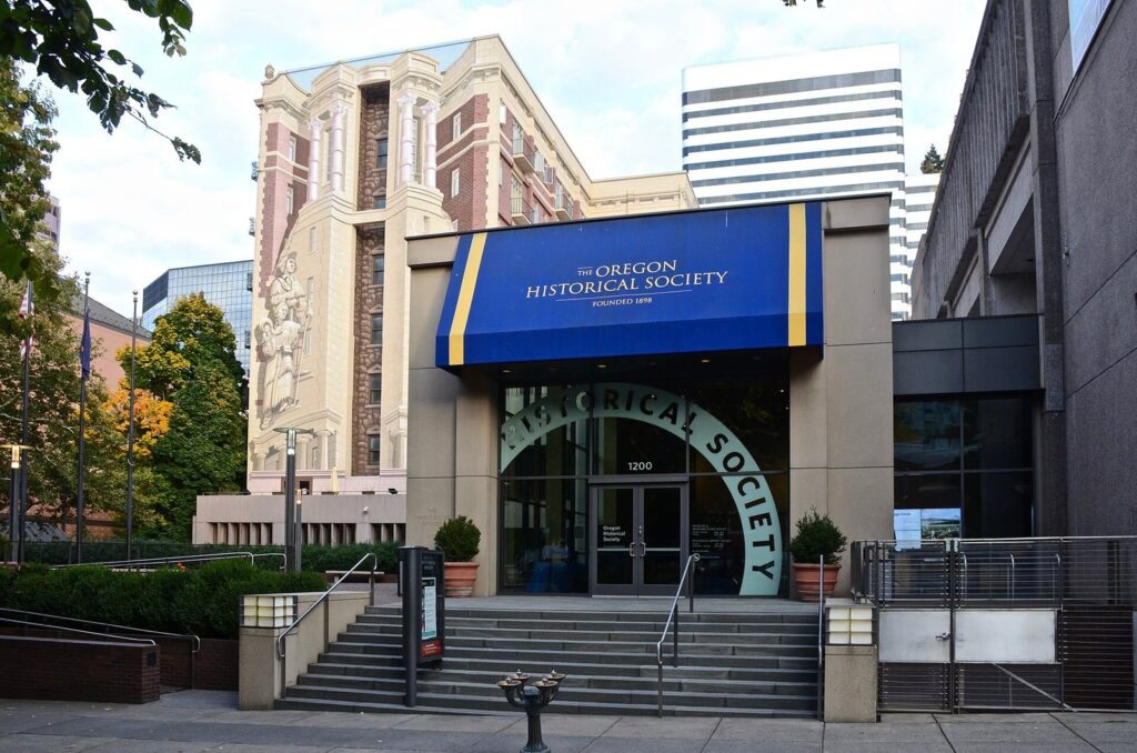 The entrance of the Oregon Historical Society under a blue awning, with painted historical figures on the tall building behind it