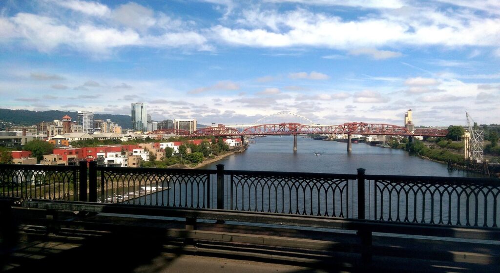 The Willamette River running north under the red trusses of the Broadway Bridge, with the Pearl District's towers on the left bank