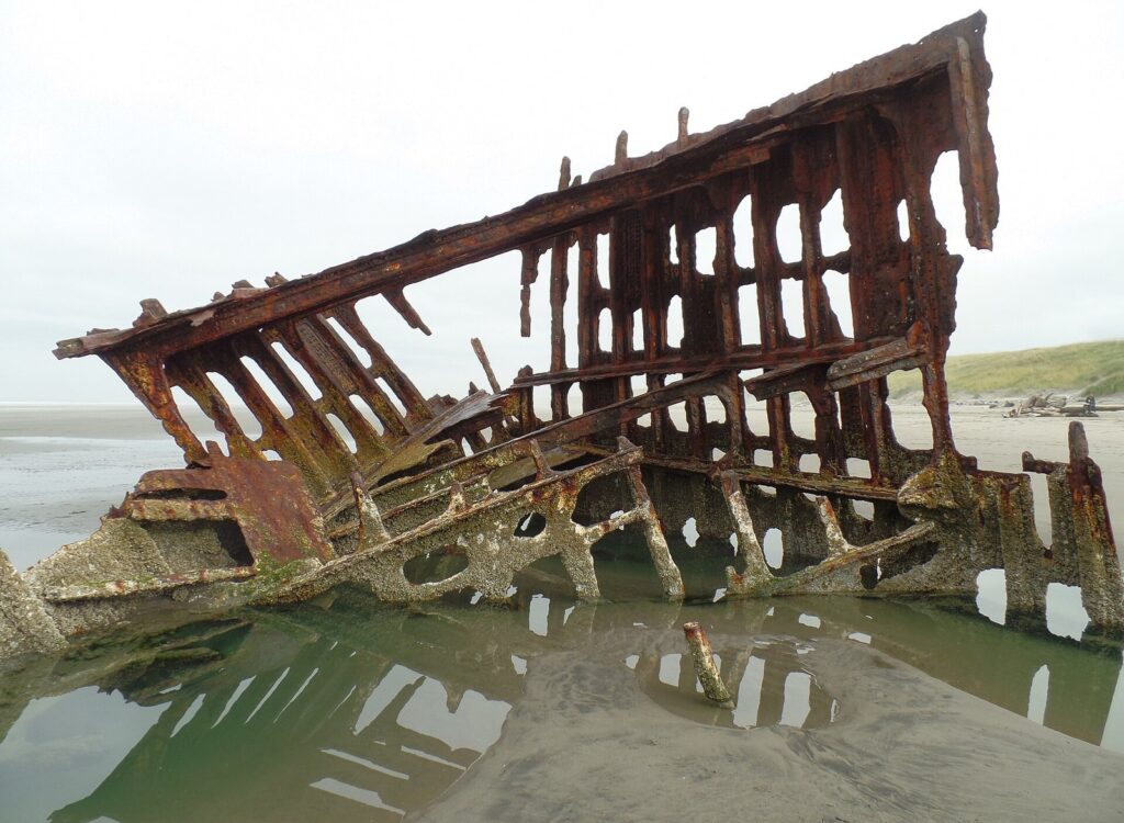 The rusted iron bow frame of a wrecked sailing ship half buried in wet sand