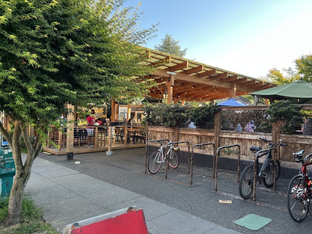 A covered wooden pavilion with picnic tables at the Prost Marketplace food cart pod, with bike racks along the sidewalk in front
