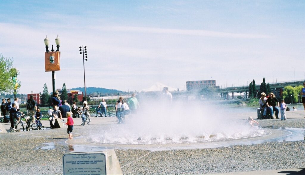 Water jets rising in a misty ring at Salmon Street Springs, with the river and snow-capped Mount Hood behind