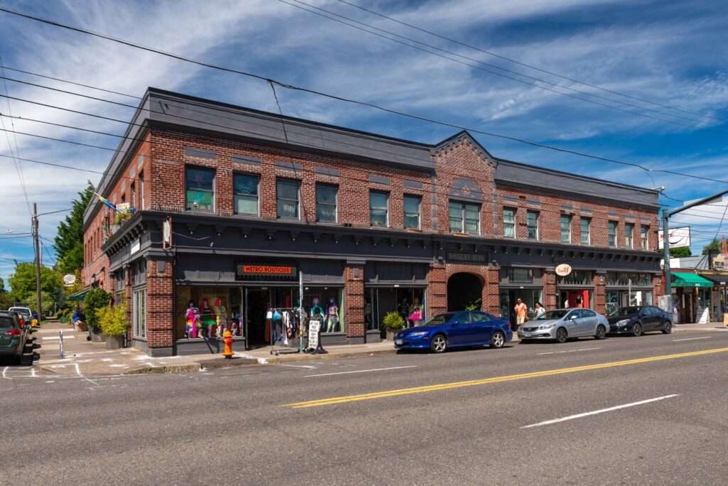 A two-story red brick commercial building with shopfronts on a corner of SE Hawthorne Boulevard under a blue sky