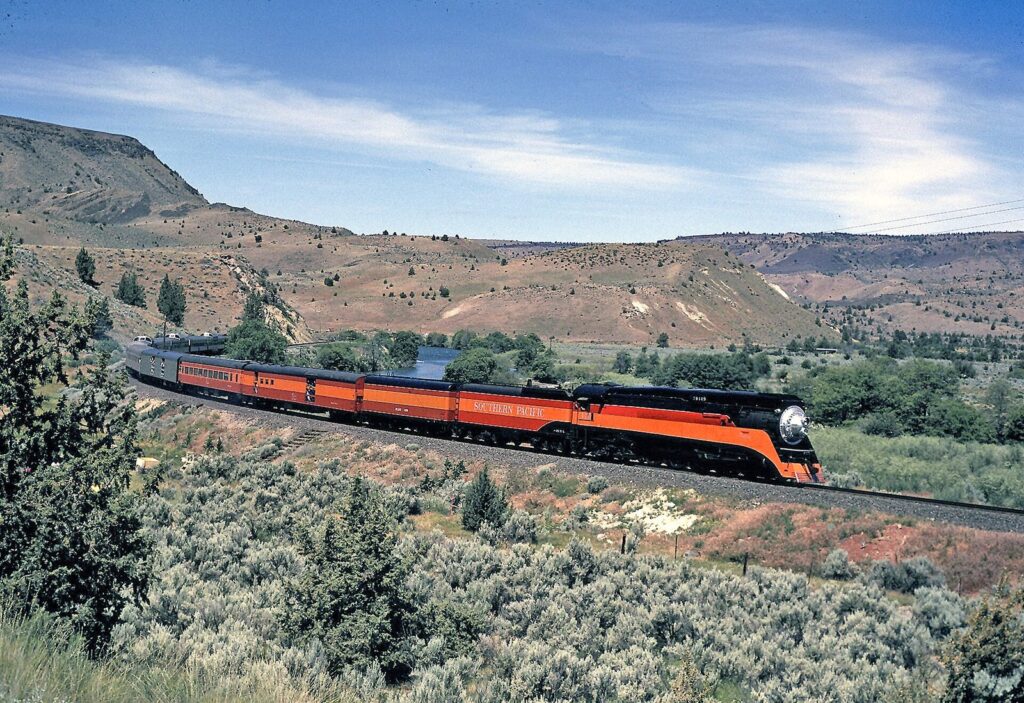 The orange and black steam locomotive Southern Pacific 4449 pulling matching passenger cars through dry hills