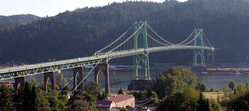 The green Gothic towers of the St. Johns Bridge crossing the Willamette River in front of a forested ridge