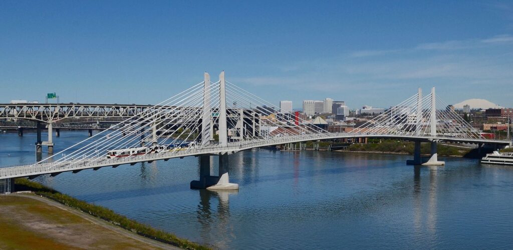 The white cable-stayed towers of Tilikum Crossing over the Willamette River, with a MAX train crossing and downtown behind