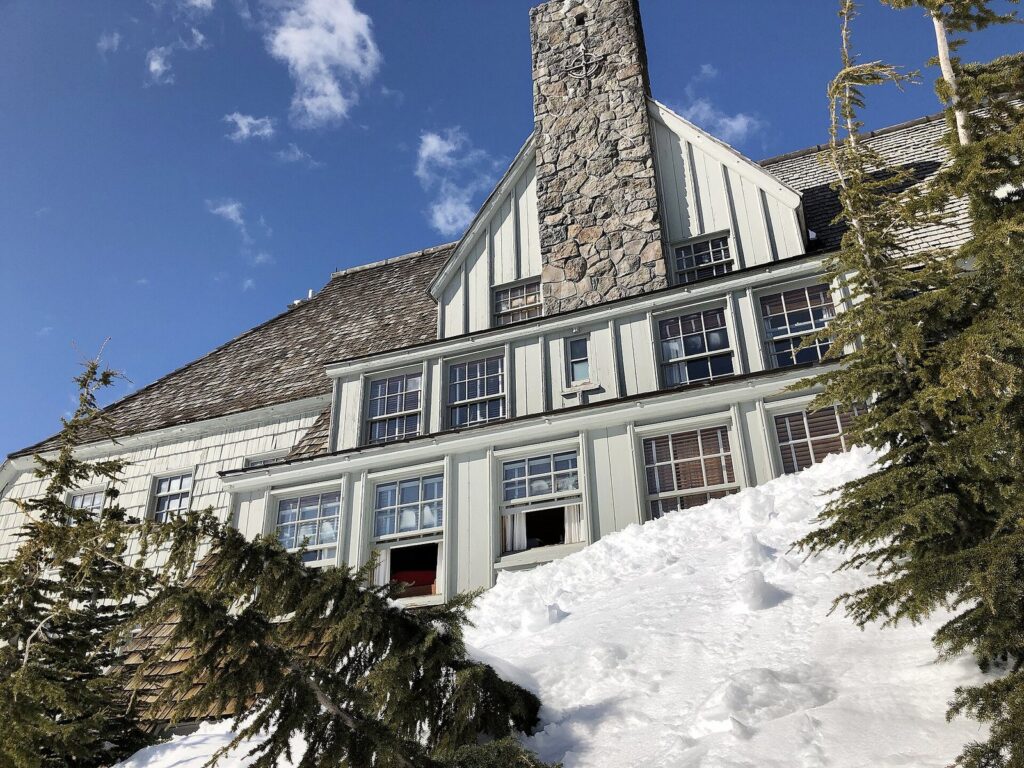 The steep gabled roof and stone chimney of Timberline Lodge's west wing above deep spring snow