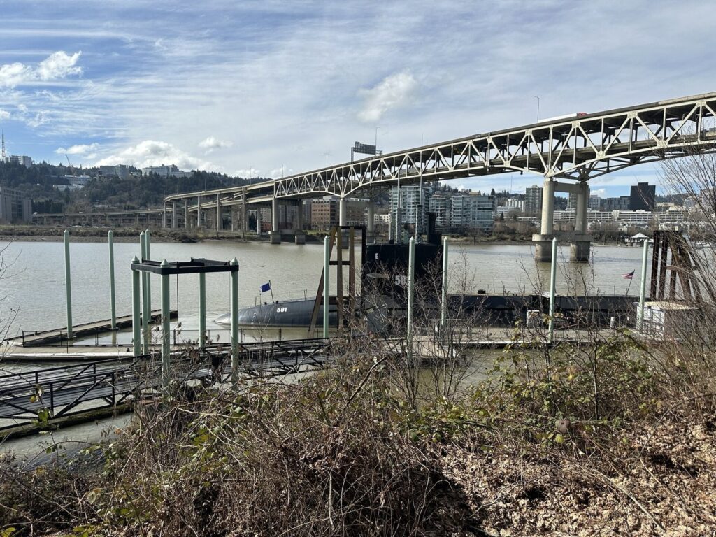 The dark hull of the USS Blueback submarine moored on the Willamette River below the Marquam Bridge