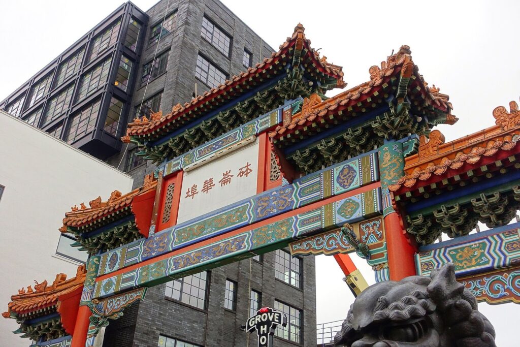 The ornate red, green and gold Chinatown gate with stone lions at its base, in front of a dark brick building