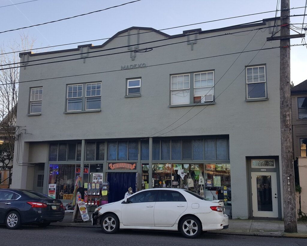 A two-story gray commercial building with shop windows full of colorful displays on a Northwest Portland street corner