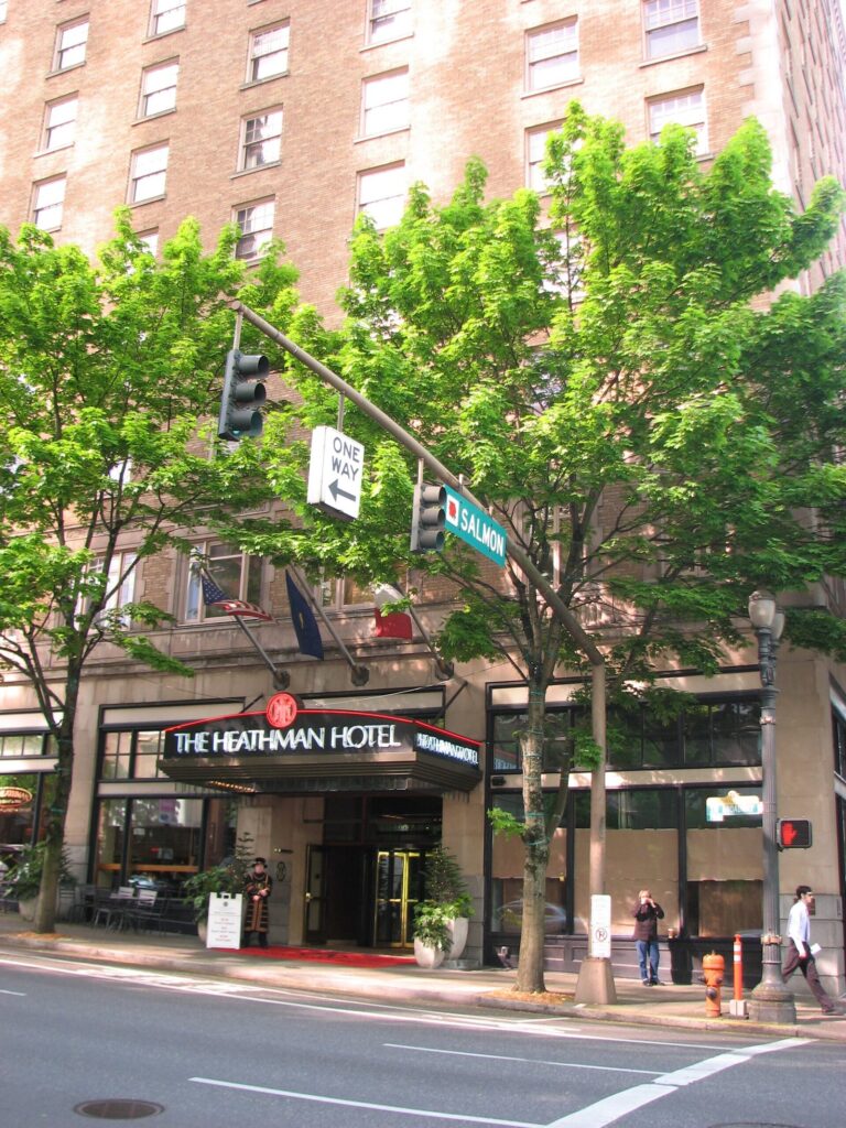 The Heathman Hotel's entrance canopy beneath a brick facade, with street trees and a traffic signal on the corner