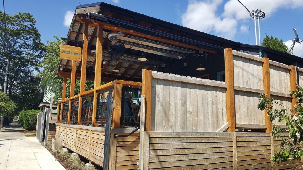 A covered wooden patio with timber posts, lattice panels and hanging lights under a blue sky