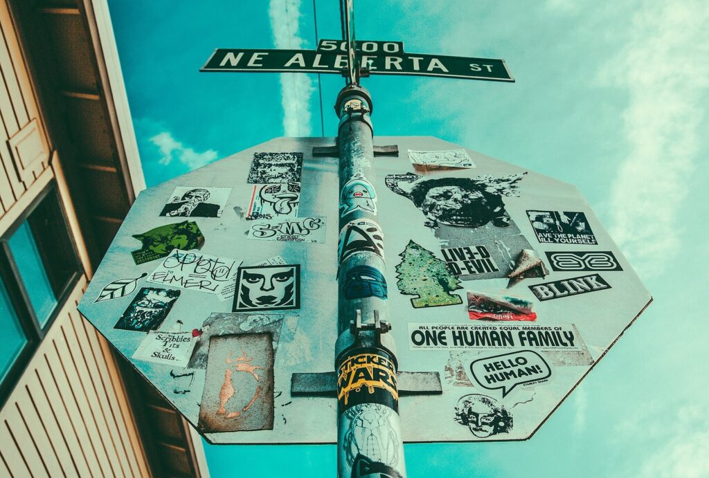 A NE Alberta St street sign above a stop sign covered in stickers, against a blue sky