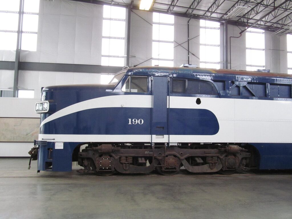 A blue and white diesel locomotive numbered 190 parked indoors on a polished concrete floor under tall windows