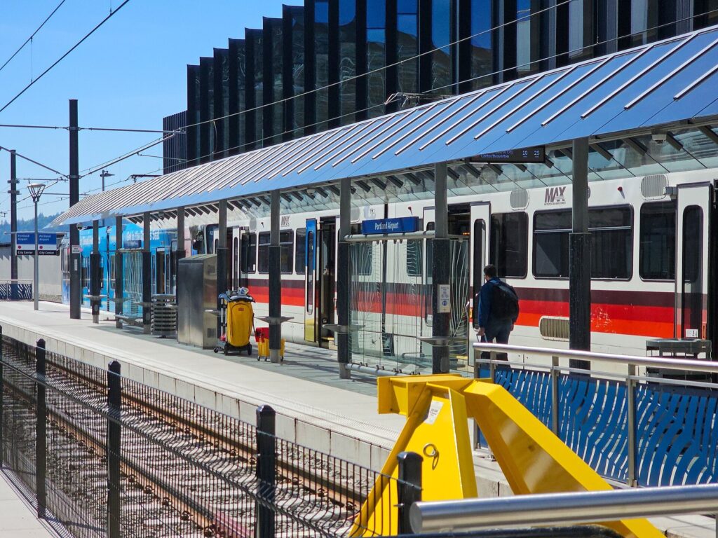 A white and red MAX train waiting under a long glass and steel canopy at the airport light rail platform