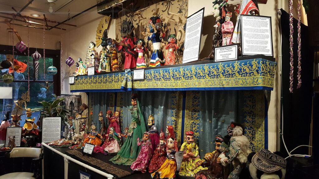 Shelves and a small stage crowded with colorful marionettes and hand puppets from around the world in a museum room