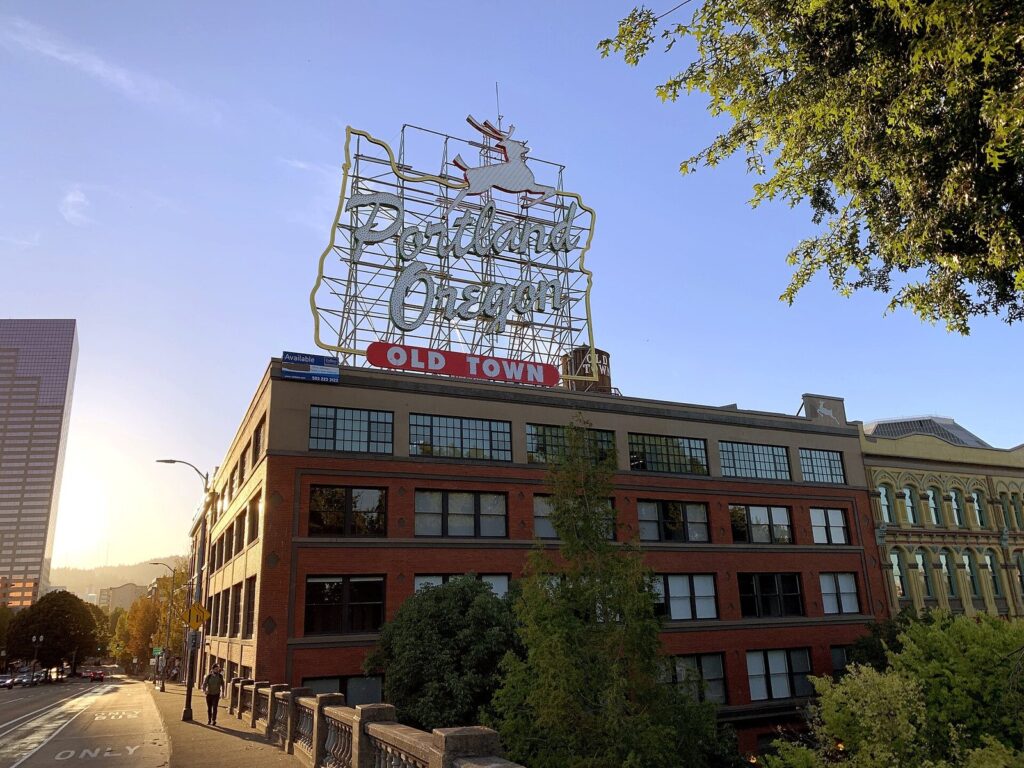 The Portland Oregon sign with its leaping white stag and red Old Town lettering on top of a brick building, lit by late sun